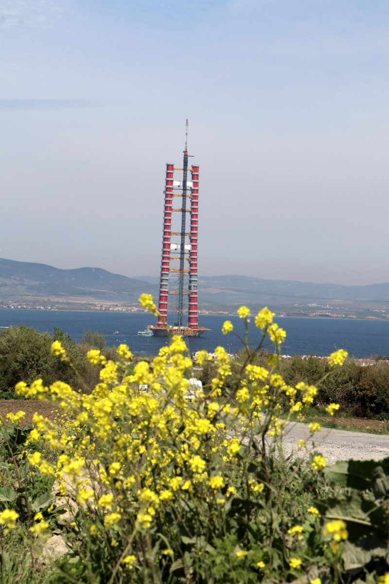 <p>1915 Çanakkale Köprüsü, tasarımındaki inceliklerle de dünyada bir ilk olmaya aday. Cumhuriyetin 100’üncü kuruluş yıl dönümünü temsil eden 2023 metrelik orta açıklığıyla, tamamlandığında dünyanın en büyük orta açıklığına sahip asma köprüsü unvanına sahip olacak 1915 Çanakkale Köprüsü’nün kule bağlantıları ve bağlantı unsurları Türk bayrağının renkleri olan kırmızı beyaza boyanacak. Her iki yakada 318 metre yüksekliğindeki kulelerin üst kısmı da Seyit Onbaşı'nın Çanakkale Savaşları'nda namluya sürdüğü top mermisini temsil edecek şekilde olacak. Köprünün 770'er metre yan açıklıklar ile birlikte toplam 3 bin 563 metre uzunluğunda olması planlanırken, 365 ve 680 metrelik yaklaşım viyadükleri ile toplam geçiş uzunluğu ise 4 bin 608 metre olacak. 2x3 trafik şeritli olacak köprünün, yaklaşık 45,06 metre genişlikte olması öngörülüyor. Köprü tabliyesinin her iki tarafında bakım onarım amacıyla kullanılacak yürüme yolları olacak. Her iki kule temeli yaklaşık 40 metre derinlikte, deniz tabanında konumlandırılacak ve çelik kule yüksekliği yaklaşık 318 metre olacak.</p>