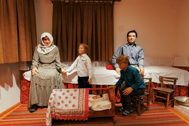 <p>Bu bölümde, Süleymanoğlu ailesinin orijinal eşyaları, annesi Hatice Hanım ile babası Süleyman Bey ve üç çocuğun silikon heykelleri, dönemsel sedir, kilim, ocak ve mutfak ögeleriyle birlikte ahşap kapı, sandık, sepet ve köy yaşamına dair unsurlar yer aldı.</p>